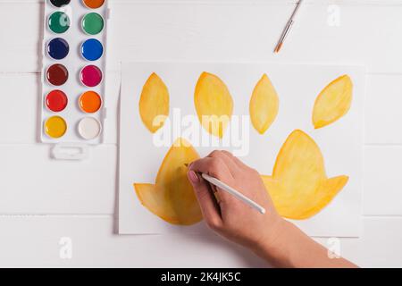 Femelle dessin à la main de feuilles d'automne de différentes formes, tailles et couleurs avec aquarelles et pinceau sur table blanche en bois. Vue de dessus. Bricoler à la main Banque D'Images