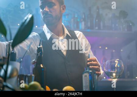 Un barman professionnel dans une chemise blanche et un tablier noir qui fait un cocktail à la fête dans une boîte de nuit tropicale. Concept de vie nocturne. Banque D'Images