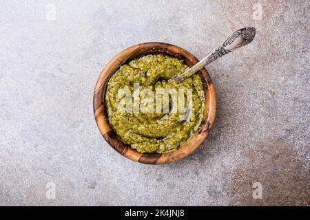 Vue de dessus de la sauce pesto dans un bol en bois comme ingrédient pour un délicieux repas de pâtes sur fond de béton gris Banque D'Images