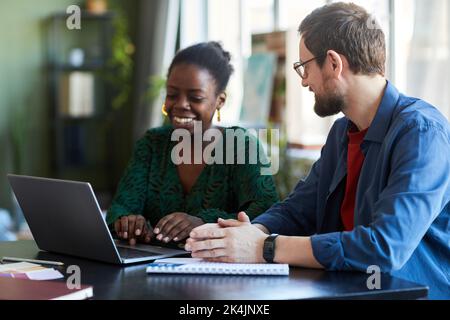 Jeune homme d'affaires regardant une collègue afro-américaine pendant son travail sur un nouveau projet d'entreprise devant un ordinateur portable lors d'une réunion Banque D'Images