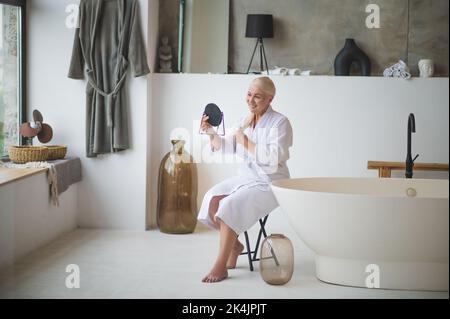 Bonne dame regardant sa coiffure dans le miroir Banque D'Images