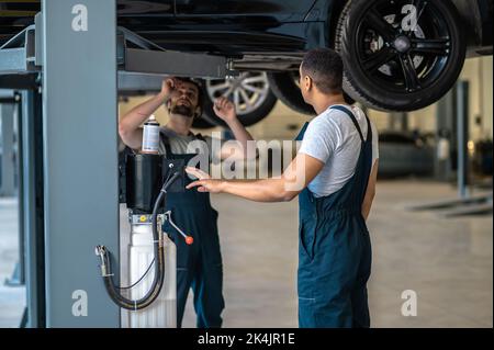 Deux mécaniciens professionnels effectuant un contrôle visuel du soubassement du véhicule Banque D'Images