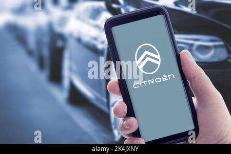Galice, Espagne; janvier 09 2021: Main tenant un smartphone avec le nouveau logo Citroën à l'écran. Voitures floues en arrière-plan Banque D'Images