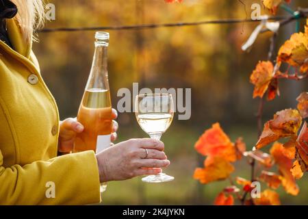Femme versant du vin blanc de la bouteille dans le verre dans le vignoble. Saison d'automne dans la cave. Dégustation de vins Vintner à l'extérieur Banque D'Images