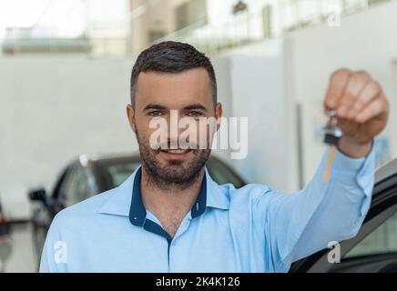 Homme souriant, client tenant des supports de clés sur le fond de la voiture dans le centre de la concession Banque D'Images