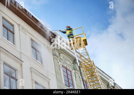 Les services publics des véhicules spéciaux retirent les glaçons des toits des maisons de la place Rynok à Lviv.Ouvriers d'hiver de toit.Grands glaçons suspendus f Banque D'Images