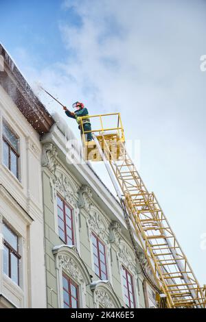 Les services publics des véhicules spéciaux retirent les glaçons des toits des maisons de la place Rynok à Lviv.Ouvriers d'hiver de toit.Grands glaçons suspendus f Banque D'Images