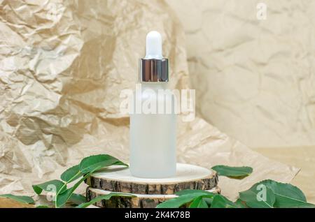 Flacon cosmétique avec pipette sur un podium en bois avec des feuilles vertes. Cosmétiques pour les soins de la peau Banque D'Images