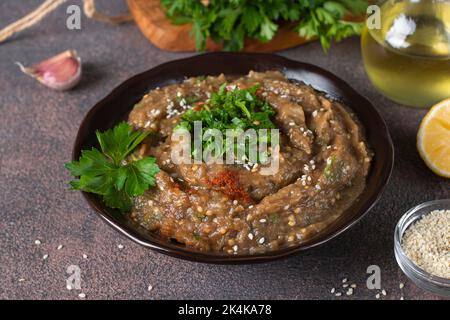 Baba ghanoush ou humus d'aubergine dans un bol sombre sur fond marron, cuisine traditionnelle du Moyen-Orient Banque D'Images