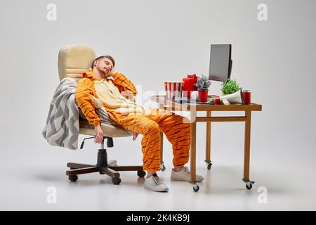Rodage. Jeune homme en costume incroyable assis au bureau d'ordinateur et dormant. Art, idées, créativité, travail et concept de vacances Banque D'Images
