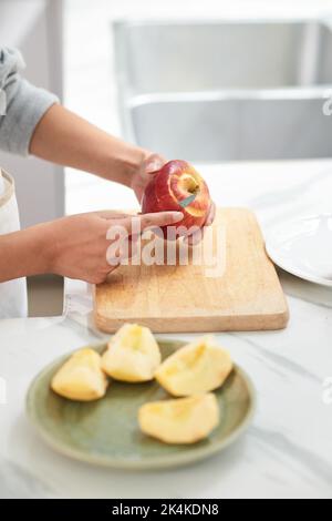 Gros plan d'une jeune femme utilisant un couteau pour couper le pelage de la pomme fraîche à la table Banque D'Images