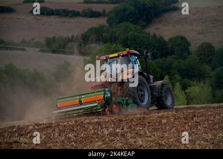 Tracteur hersant un sol brun rougeâtre, poussiéreux et argileux dans un paysage vallonné Banque D'Images