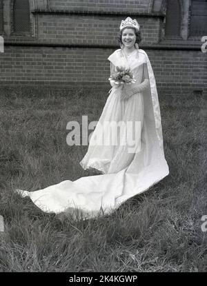 1959, historique, une adolescente, la reine locale de mai, debout pour sa photo dans sa longue robe, avec des fleurs et couronne sur la tête, Leeds, Angleterre, Royaume-Uni. Sa photo est prise dans le parc de l'église avant le carnaval où elle sera une figure importante dans les célébrations traditionnelles du jour de mai, un ancien festival européen marquant le début de l'été. Banque D'Images