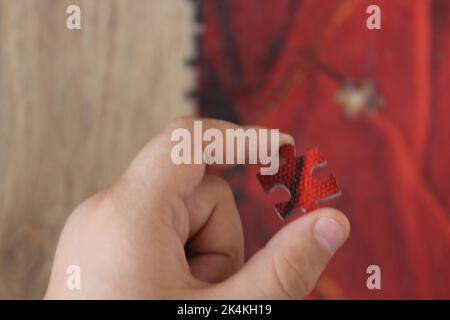 Un garçon tenant une pièce de puzzle rouge pour la mettre en place. Idée de concept de scie sauteuse. Banque D'Images