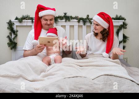 Femme en colère donnant gadget à l'enfant sur le lit décoré pour noël et nouvel an, couple de famille dans la chambre à la maison - Moscou, Russie, 27 décembre 2021 Banque D'Images