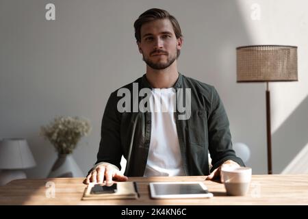 Un employé de bureau du millénaire qui a l'air bien assis à son bureau souriant en regardant l'appareil photo. Travailleur réussi, avancement de carrière et opportunité, propriétaire de PROSPER Banque D'Images