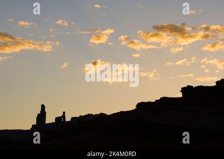 Silhouettes au coucher du soleil de Monster Tower et de Washer Woman Arch le long du White Rim Trail dans le parc national de Canyonlands, Utah. Banque D'Images