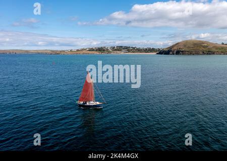 Un bateau à voile à l'ancienne avec une voile rouge flottant sur l'océan dans l'estuaire de la Camel près de Padstow dans les Cornouailles Banque D'Images