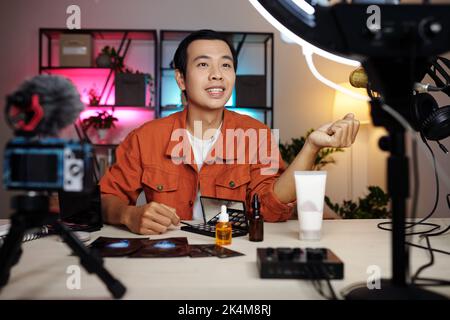 Portrait horizontal moyen sélectif de focus de beau jeune homme asiatique enregistrement de contenu pour le blog vidéo faisant l'examen des produits de beauté Banque D'Images