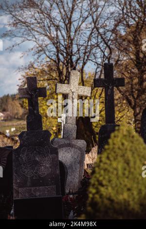 La vieille pierre traverse sur les tombes dans un ancien cimetière de Lituanie avec une des croix au milieu illuminée par la lumière du soleil, verticale Banque D'Images