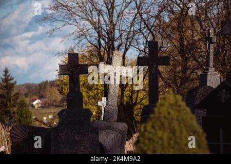 La vieille pierre traverse sur les tombes dans un ancien cimetière de Lituanie avec une des croix au milieu illuminée par la lumière du soleil Banque D'Images