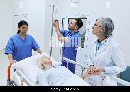 Infirmière mettant goutte à goutte sur un patient âgé allongé sur un brancard pendant qu'il est examiné par une femme médecin expérimentée. les assistants médicaux emmèneront la femme blessée Banque D'Images
