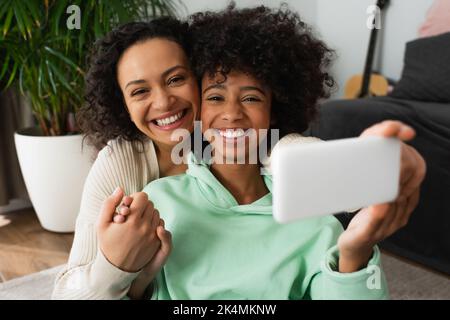 joyeuse mère afro-américaine prenant selfie avec fille joyeuse de préadolescence sur smartphone, image de stock Banque D'Images