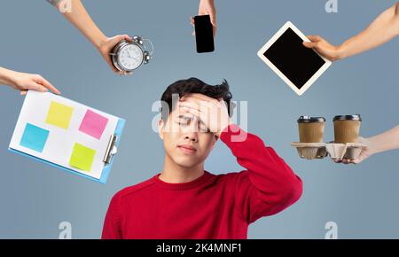 Homme asiatique épuisé entouré de mains avec des gadgets Banque D'Images