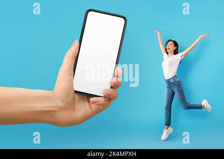 Heureuse excitée jeune femme européenne dans le saut occasionnel, hurlant, regarde l'énorme smartphone avec écran vide Banque D'Images