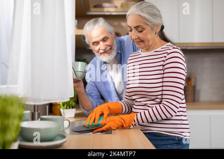 Concept de ménage. Souriant mari et femme sénior lave les plats ensemble dans la cuisine Banque D'Images