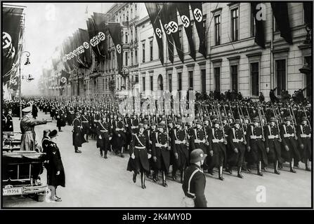 Leibstandarte Waffen SS Adolf Hitler dans son haut ouvert Mercedes Motorcar salue un défilé de son régiment personnel de garde du corps, la 1st SS Division Leibstandarte Waffen SS avec des bâtiments encorchés avec des drapeaux swastika 30 janvier, 1937 Banque D'Images