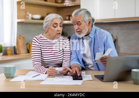 Couple senior assis à la table avec des papiers et des factures et en utilisant la calculatrice Banque D'Images