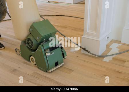 C'est un processus où dans une maison nouvellement construite une ponceuse de plancher est utilisée pour meuler un plancher de parquet à l'aide d'un outil de ponçage Banque D'Images