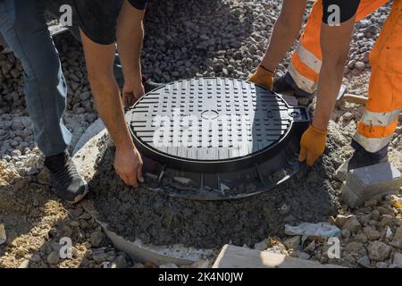 Une trappe d'égout en fonte est installée dans un puits en béton, en préparation de l'installation d'un puits d'égout dans le sol. Banque D'Images