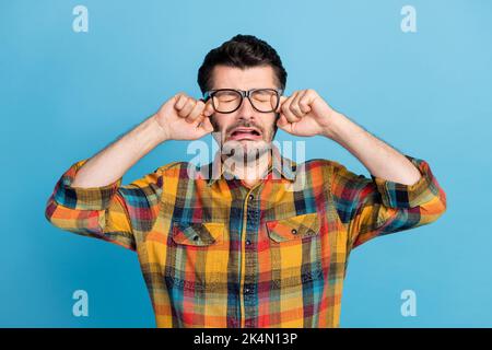 Photo de triste brunet Guy pleurant porter lunettes chemise à carreaux isolée sur fond bleu Banque D'Images