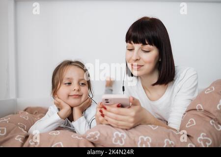 Gros plan de maman souriante et petite fille se détendre dans un lit confortable lire drôle intéressant enfants réserver ensemble, la mère heureuse et petite fille d'avant-goût profiter du repos de conte de fées dans la chambre confortable Banque D'Images