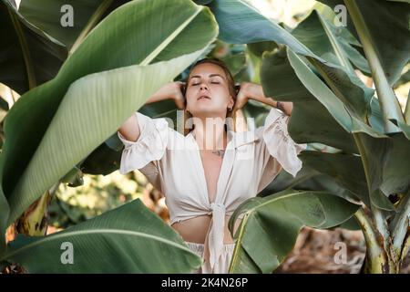 Belle femme dans la jungle. Un centre de villégiature ou un hôtel avec des arbres et des plantes tropicaux. Femme avec près de la feuille de banane. Fille en vacances dans la forêt tropicale Banque D'Images