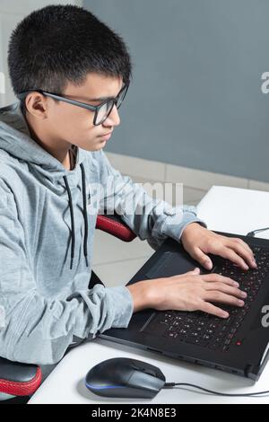 Adolescent garçon à la maison école étudier chambre bureau pc ordinateur lunettes assis regardant les devoirs Banque D'Images