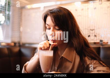 Une jeune femme boit du milk-shake au chocolat au restaurant Banque D'Images