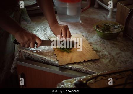 Une femme coupe l'aneth vert sur une planche à découper en bois dans la cuisine Banque D'Images