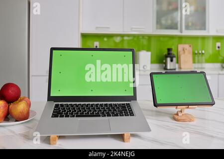 Deux gadgets mobiles sans fil avec croix noires sur écrans verts sur des supports en bois sur une table de cuisine en marbre blanc Banque D'Images