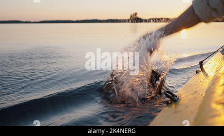 Une personne excitée se délasse de la voile sur la rivière au coucher du soleil. L'homme dérive sur un bateau jaune en plongeant la main dans l'eau. Eau calme lave gars main Banque D'Images