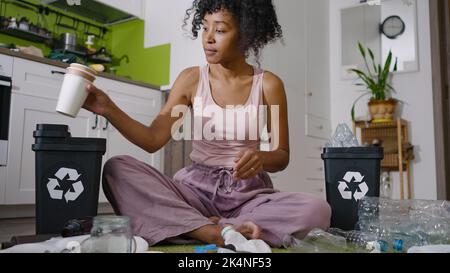 Une femme afro-américaine trie les déchets en plastique dans des poubelles pour les recycler. La jeune femme au foyer s'occupe de l'environnement et de l'écologie Banque D'Images