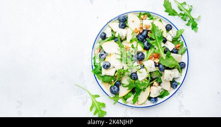 Delicious arugula salad with pears, blueberries, roquefort cheese and walnuts. Black kitchen table background, top view Banque D'Images