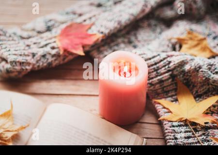 Bougie brûlante, livre ouvert, feuilles d'automne et pull tricoté sur table en bois. Concept d'automne. Vue de dessus. Banque D'Images