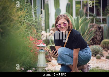 belle femme asiatique tenant un smartphone souriant dans le jardin de la maison Banque D'Images