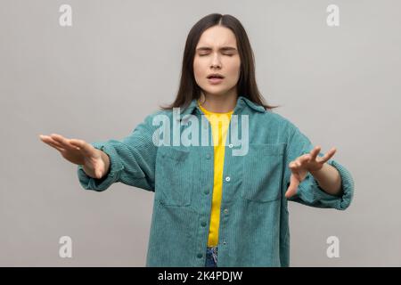 Je ne peux pas voir. Portrait d'une femme marchant avec des mains tendues, aveugle ou désorientée dans l'obscurité, ayant des problèmes de vue, portant une veste de style décontracté. Prise de vue en studio isolée sur fond gris. Banque D'Images