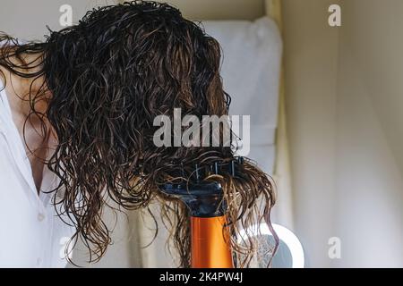 Femme diffuse ses cheveux avec un sèche-cheveux. Séchage des cheveux selon une méthode de coiffage en courbure Banque D'Images