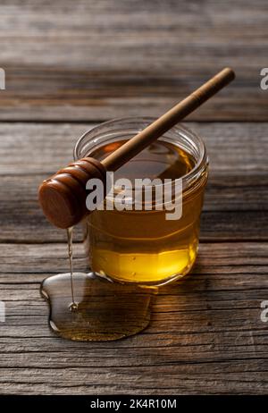 Miel et miel en bois en récipient en verre sur fond de bois ancien. Le miel s'égoutte du balancier de miel. Banque D'Images