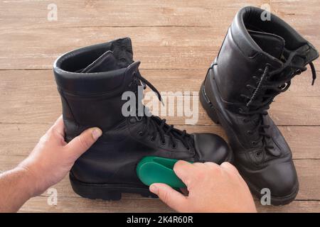 Image des mains d'un homme qui polit une paire de bottes militaires avec une brosse à chaussures. Banque D'Images